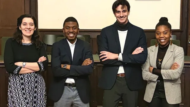 Vier Personen stehen mit verschränkten Armen vor einer Holzwand in einem Raum