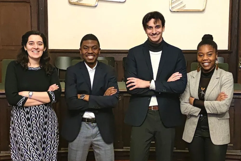 Vier Personen stehen mit verschränkten Armen vor einer Holzwand in einem Raum