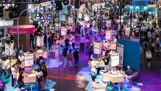 Große Messehalle mit zahlreichen Ständen und vielen Besuchern, die sich zwischen den Ausstellungsflächen bewegen