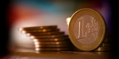 Nahaufnahme einer 1-Euro-Münze vor einem Stapel weiterer Münzen auf einer Oberfläche