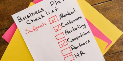 Checkliste für einen Businessplan mit abgehakten Punkten Market, Customers und Partners auf einem weißen Blatt Papier auf buntem Hintergrund