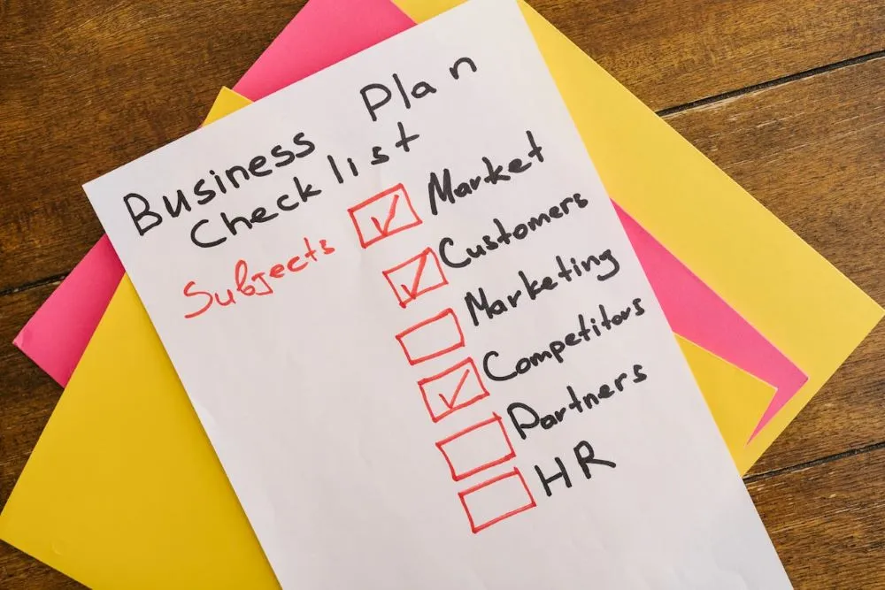 Checkliste für einen Businessplan mit abgehakten Punkten Market, Customers und Partners auf einem weißen Blatt Papier auf buntem Hintergrund